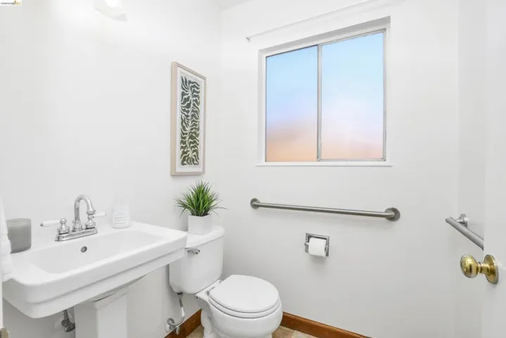 Well-lit half-bathroom featuring a pedestal sink with chrome faucet, a white toilet, and a window with frosted privacy glass
