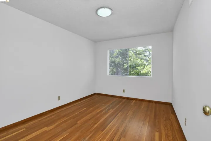 Room featuring wood-finish flooring, white painted walls, a window with horizontal blinds, and a flush mount ceiling light