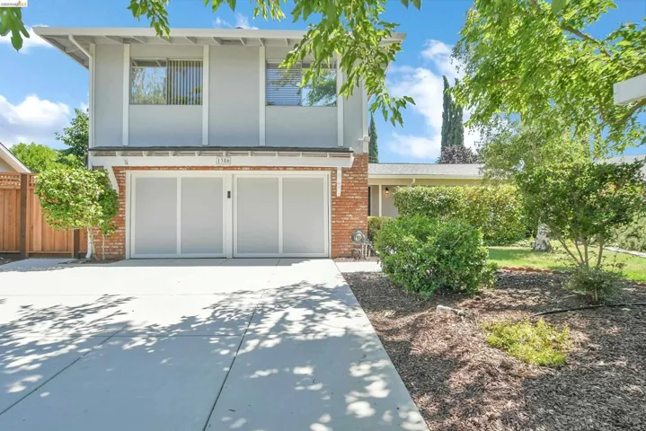 Two-story residence featuring a light gray exterior with brick accents, dual garage doors, a concrete driveway, and established front landscaping