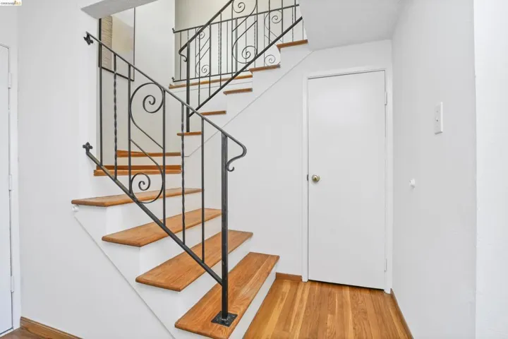 Staircase featuring wood-finish treads, white risers, and wrought iron railings