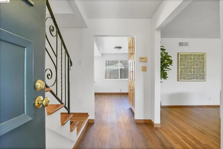 Entryway featuring a dark paneled door with brass hardware, wood-finish flooring, a staircase with wrought iron railing, and built-in wood cabinetry
