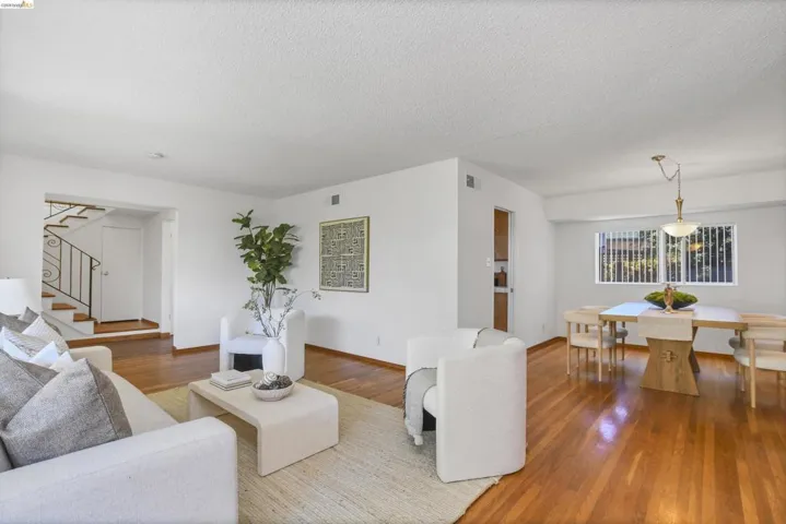 Open-concept living space featuring wood-finish flooring, white walls, and a staircase with an ornamental wrought-iron railing