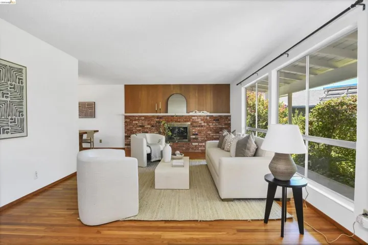Spacious living area featuring expansive windows, wood-finish flooring, a brick fireplace with a wood mantle, and a recessed wood panel wall