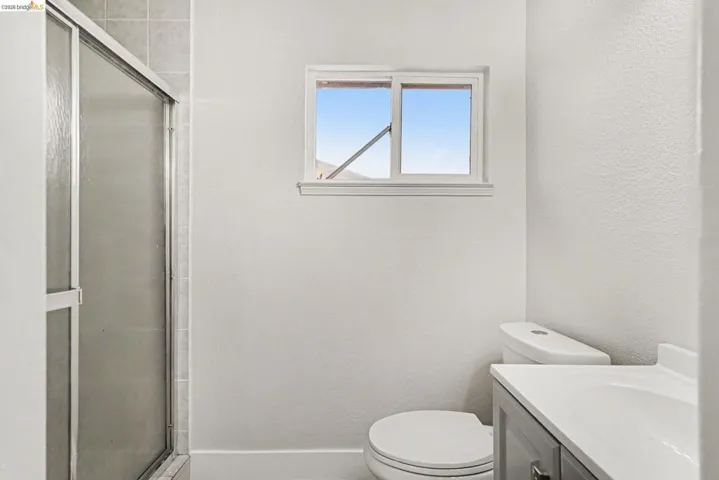 Bathroom featuring a glass-enclosed shower, white toilet, and single-pane window