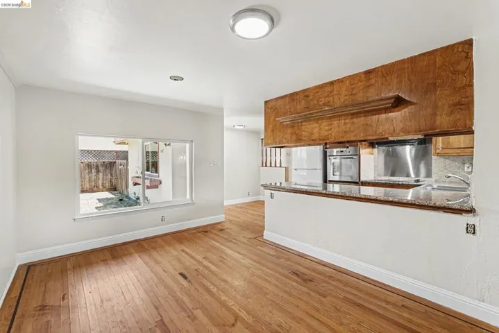 Open-concept room featuring wood-finish flooring, a pass-through kitchen with granite-style countertops, stainless steel appliances, and a built-in oven