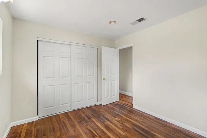 Room featuring wood-finish flooring, white walls, and a large closet with bifold doors