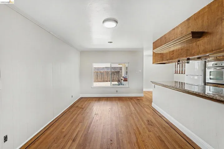 Open-concept living space featuring wood-finish flooring, white paneled walls, and a recessed window