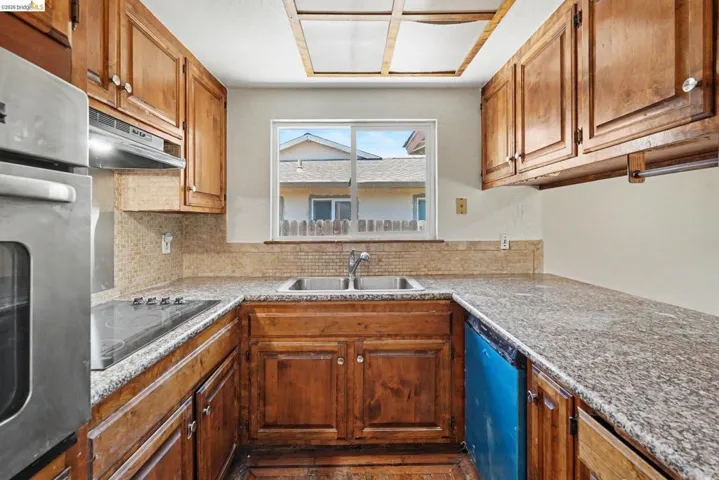 Kitchen featuring wood cabinetry, granite-style countertops, stainless steel wall oven, and electric cooktop