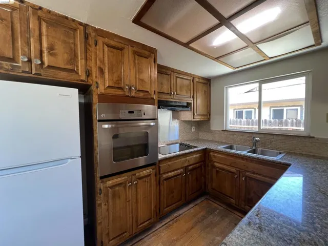 Kitchen featuring wood cabinetry, stainless steel built-in oven, granite-look countertops, and a full tile backsplash