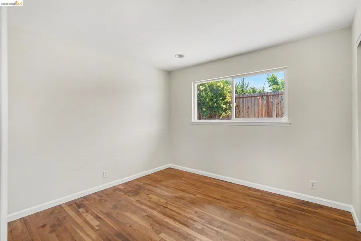 Light-filled room featuring wood-finish flooring, neutral wall tones, white baseboards, and a recessed ceiling light