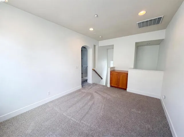 Carpeted room featuring recessed lighting, a built-in wood-finish cabinet, an arched doorway, a staircase with a handrail, and a white baseboard trim