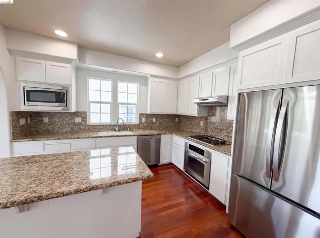 Kitchen featuring white cabinetry, granite countertops, stainless steel appliances, wood-finish flooring, and recessed lighting