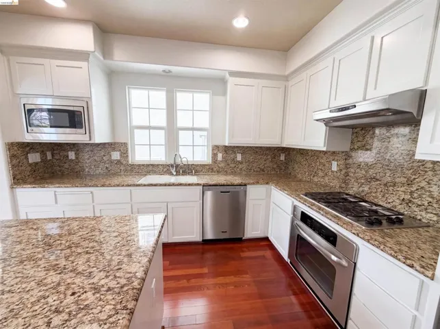 Kitchen featuring wood-finish flooring, white cabinetry, granite countertops, stainless steel appliances, and an integrated kitchen island