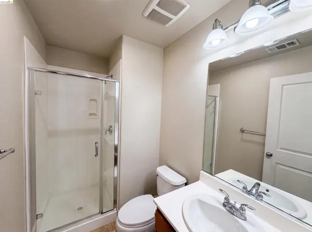 Bathroom featuring a walk-in shower with clear glass enclosure, white vanity countertop with integrated sink, chrome faucet, and overhead vanity lighting