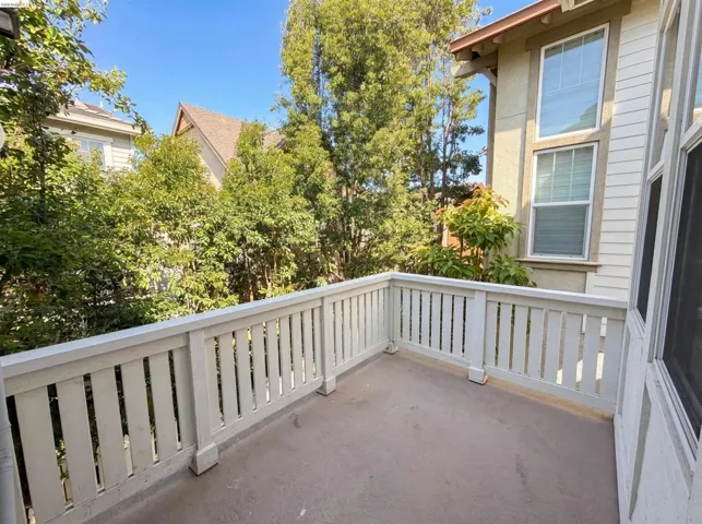 Outdoor balcony featuring a painted wood railing, a solid surface floor, and surrounding mature trees