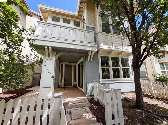 Traditional-style exterior featuring a second-story balcony with white railing, a ground-level covered entry, multiple large pane windows, and a decorative picket fence