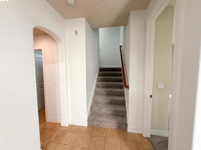 Carpeted staircase with wood handrail, featuring a tile flooring entry, arched doorway, and white trim