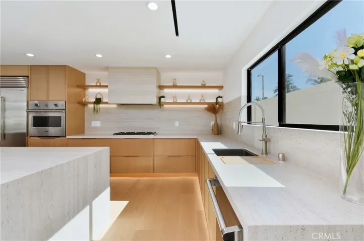 Bright and inviting gourmet kitchen showcasing a large picture window, illuminated floating shelves, custom wood cabinetry, and premium finishes throughout