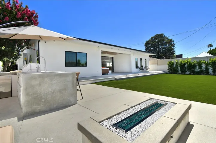 Angled view of the backyard showcasing seamless indoor=outdoor living, a spacious lawn, outdoor kitchen, and a contemporary fire pit that provides warmth and ambiance for year-round entertaining