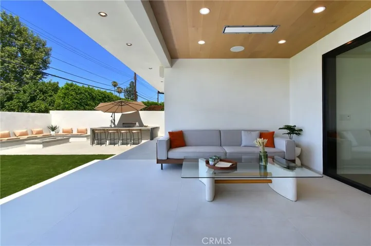 Spacious covered outdoor lounge space featuring a built-in surround sound system, ceiling heater, and seamless views of the beautifully landscaped backyard.