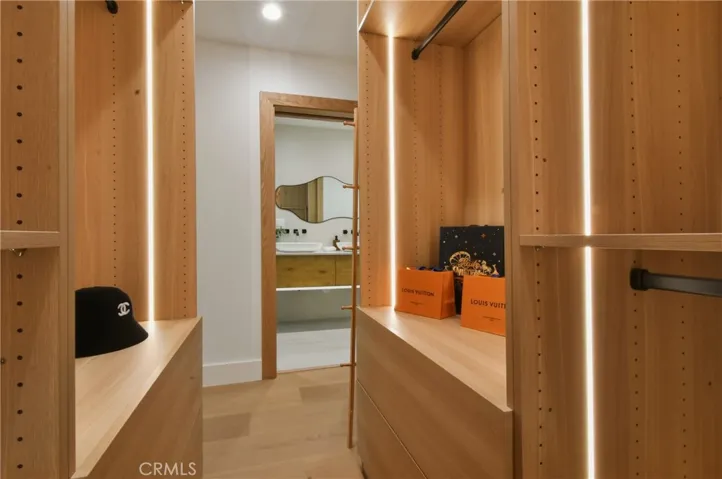 Custom walk-in closet space with beautiful built-in wood shelving and integrated storage, with integrated LED-lit shelvings