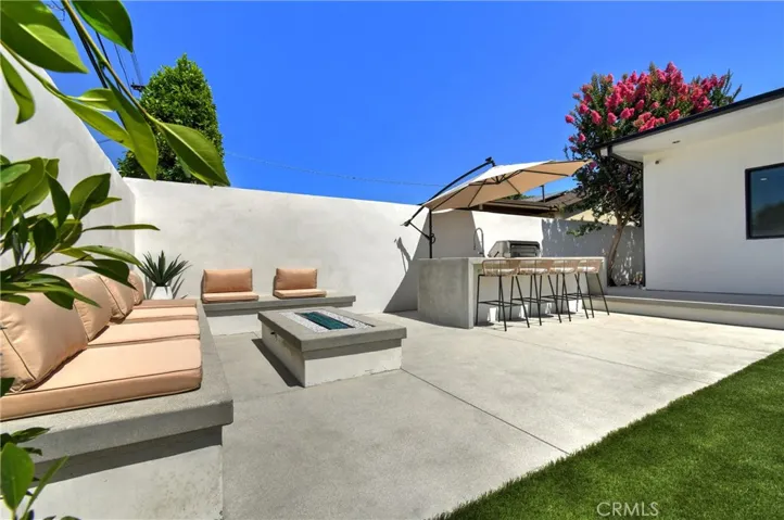 Built-in outdoor lounge seating with a contemporary fire pit, and a fully equipped outdoor kitchen featuring a built-in BBQ, sink with faucet, and under-counter refrigerator - creating the perfect space for relaxing and entertaining
