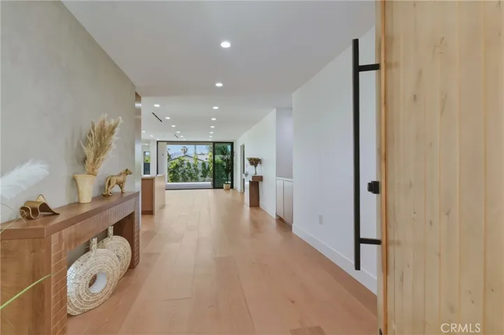 An inviting, wide-set entry foyer showcasing a striking modern pivot door, gorgeous warm wood flooring and an expansive open-concept transition.