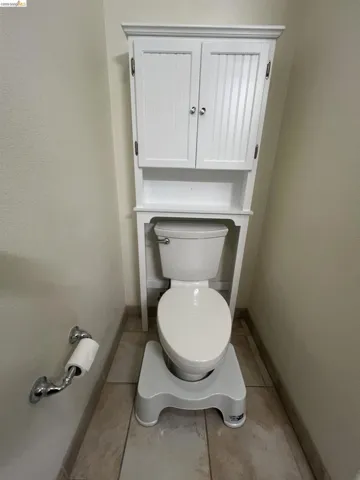 Bathroom featuring tile flooring and an over-the-toilet storage cabinet with beadboard cabinet doors and chrome hardware