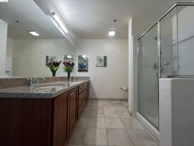 Spacious bathroom featuring a dual vanity with a speckled countertop, brown wood cabinetry, chrome faucets, and tile flooring