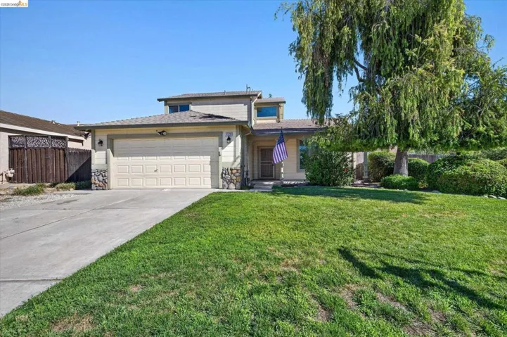 Two-story residence featuring a two-car garage, stone veneer accents, and a mature front yard tree