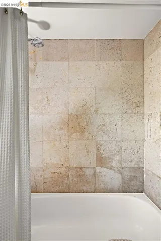 Bathtub and shower combination featuring natural stone-look tile surround and a chrome shower head