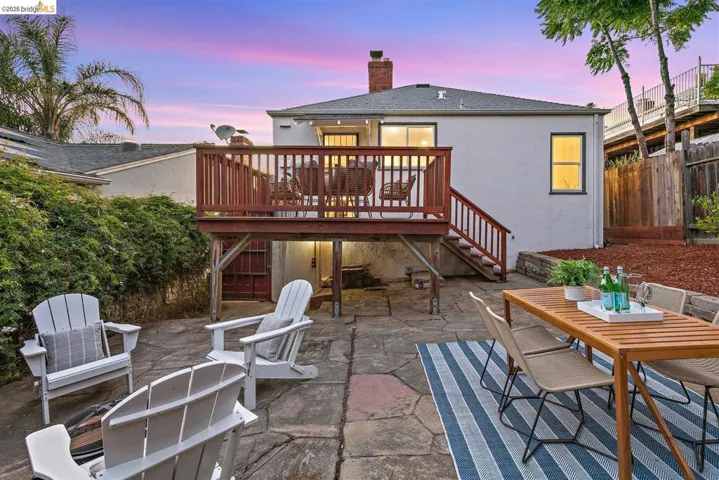 Rear exterior featuring a raised wooden deck with railings, a stone patio, and perimeter landscaping
