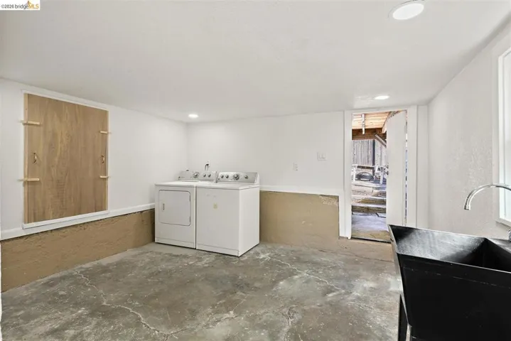 Utility room featuring a concrete floor, recessed lighting, and a dark basin sink with a chrome faucet