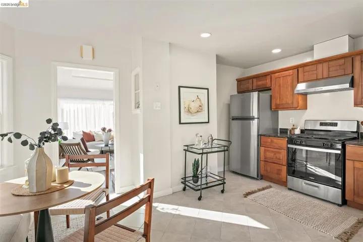 Kitchen featuring wood cabinetry, stainless steel appliances, dark countertops, and light tile flooring