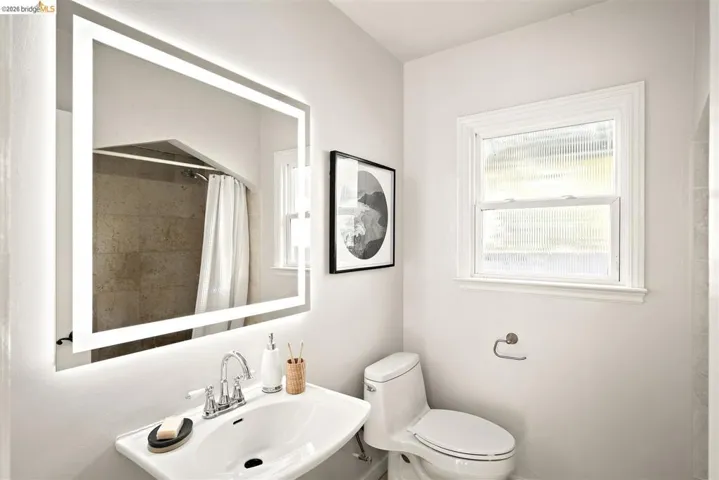 Modern bathroom featuring a lighted vanity mirror, pedestal sink with dual-handle faucet, and a toilet with a dual-flush mechanism