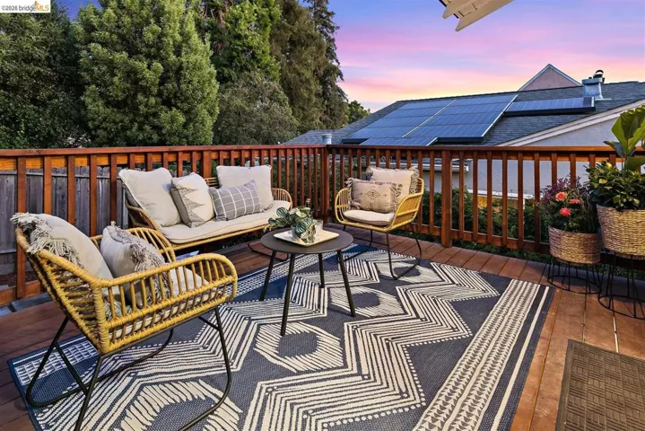 Expansive exterior wood deck featuring a wood railing, decorative area rug, and mature tree backdrop