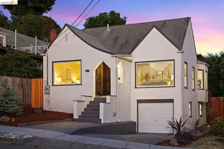 Stucco exterior with a peaked roofline, arched entry, prominent front windows, and a lower-level garage