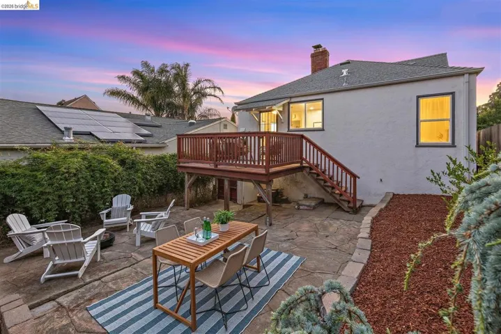 Rear exterior featuring a raised wooden deck with stairs, a flagstone patio, and a mulched garden bed