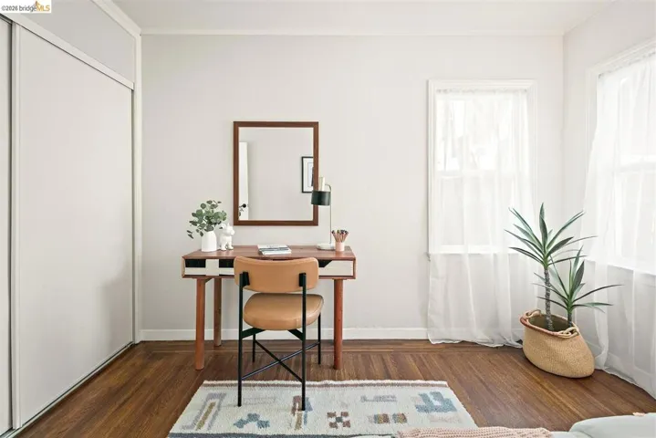 Neutral-toned room featuring a built-in closet with sliding doors, two windows with white trim, and wood-finish flooring