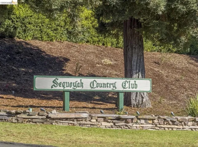 "Sequoyah Country Club" signage framed by a mature tree and a stone retaining wall
