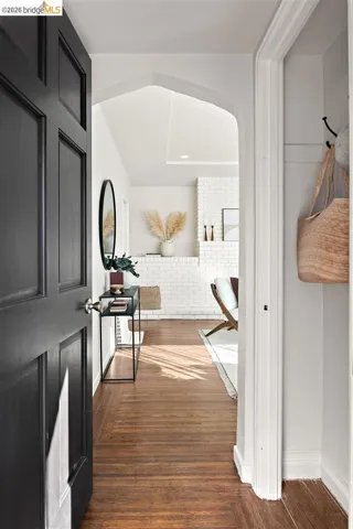 Dark paneled entry door opens to a wood-finish flooring hallway with a vaulted ceiling