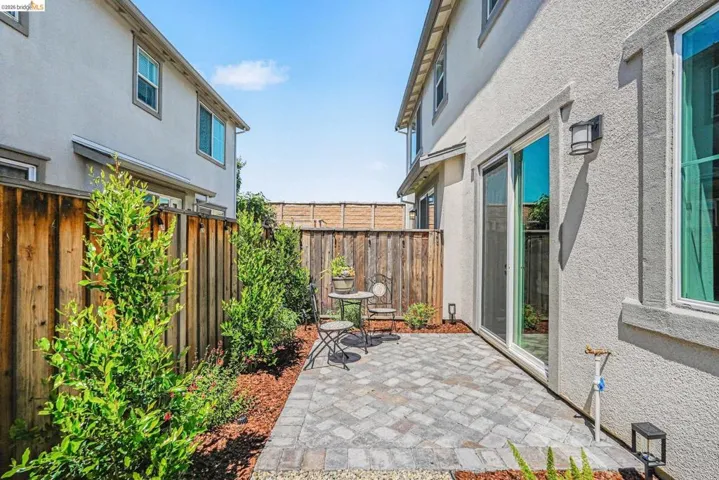 Private patio area featuring a paver stone surface, mature perimeter landscaping, and a wood fence enclosure
