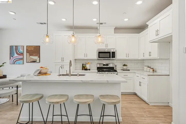 Modern kitchen featuring white shaker cabinetry, stainless steel appliances, a subway tile backsplash, and a large island with integrated seating
