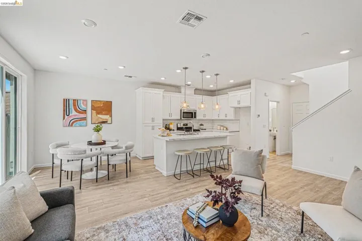 Open-concept living space featuring wood-finish flooring, recessed lighting, and a white kitchen with shaker cabinetry and a large island