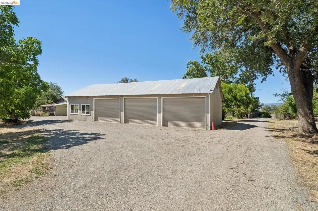 Three-bay garage structure with a gravel driveway and surrounding mature trees