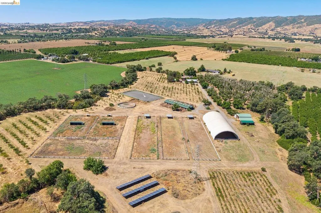 Expansive rural property featuring multiple agricultural fields, a large covered structure, and solar panel arrays