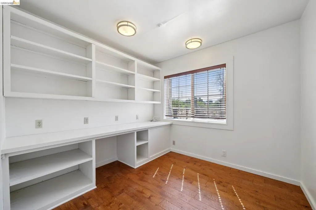Room featuring built-in white cabinetry, integrated desk space, and wood-finish flooring