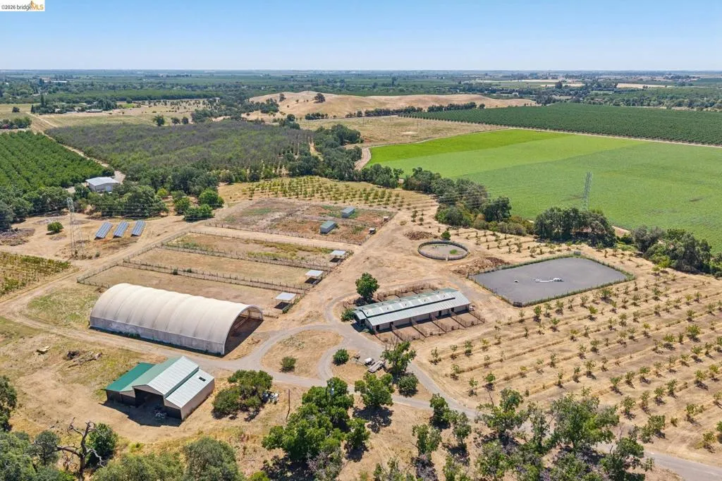 Expansive agricultural property featuring multiple fenced paddocks, a large covered arena, and a dedicated barn structure