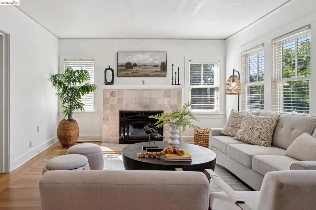 Living area featuring wood-finish flooring, a tiled fireplace with a black insert, white walls, and multiple windows with blinds