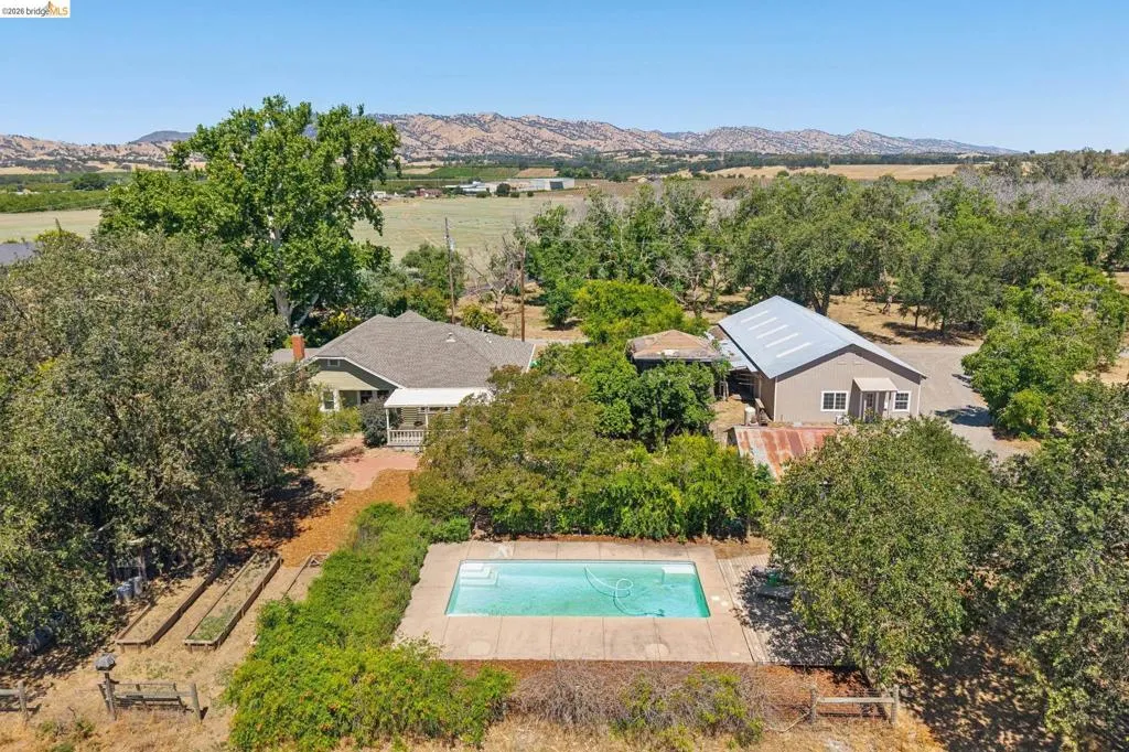 Expansive property featuring a rectangular swimming pool with concrete surround, a detached auxiliary structure with a metal roof, and a single-story residence with a covered porch
